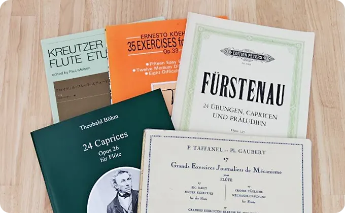 木製のテーブルの上に、フルートの練習曲やエチュードの楽譜が複数並べられている