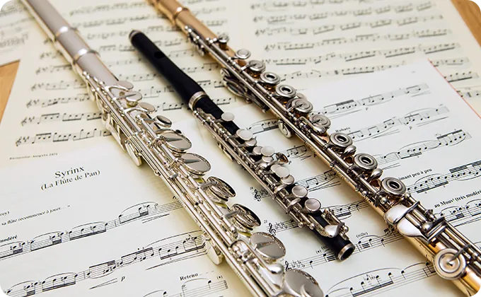 複数のフルートとピッコロが楽譜の上に並べられているクローズアップ写真